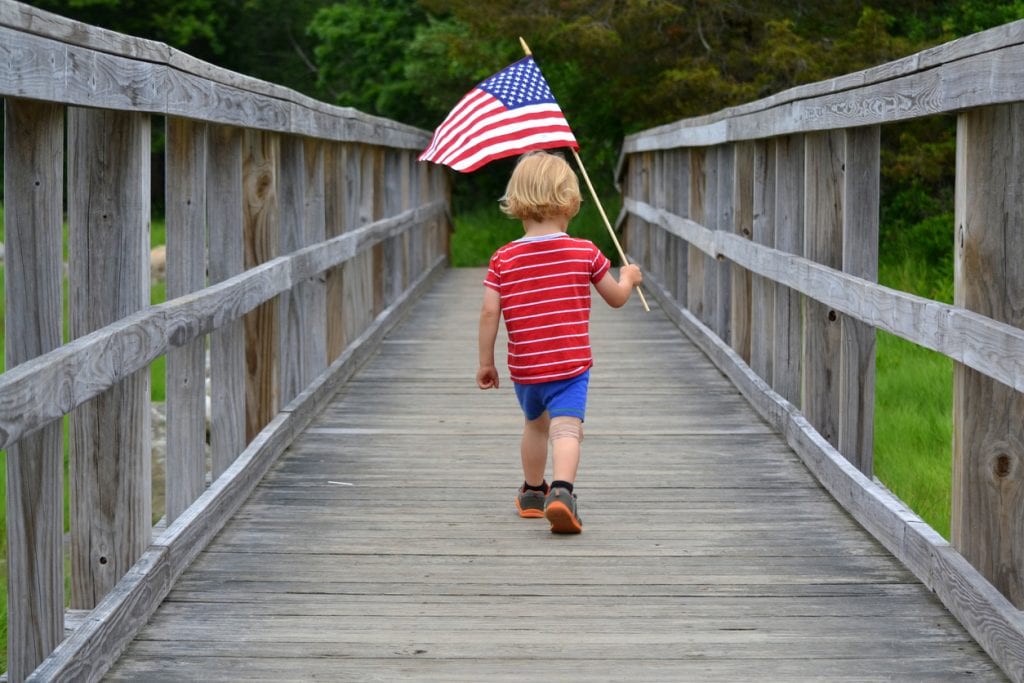 Young boy holding American flag on wood bridge